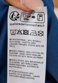 Tvättrådsetikett på blått tyg, som visar tvättanvisningar och sammansättning: 95 % bomull, 5 % elastan, på flera språk.
