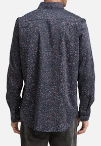 Chemise navy avec un motif moucheté en blanc, rouge et bleu. Manches longues, col classique, poignets à boutons et ourlet arrondi.