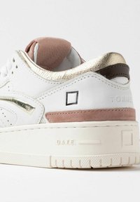 Hvide sneakers med en gylden metallic detalje, blød lyserød suede hæltab, struktureret hvid læder og en tyk, hvid gummisål.