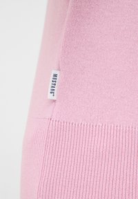 Hellrosa gestrickter Pullover mit glatter Textur, geripptem Saum und einem weißen Markenetikett an der Seitennaht.