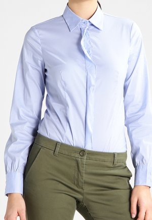 Camicia azzurra chiaro con colletto a punta, maniche lunghe e vestibilità aderente, abbinata a pantaloni verdi oliva.