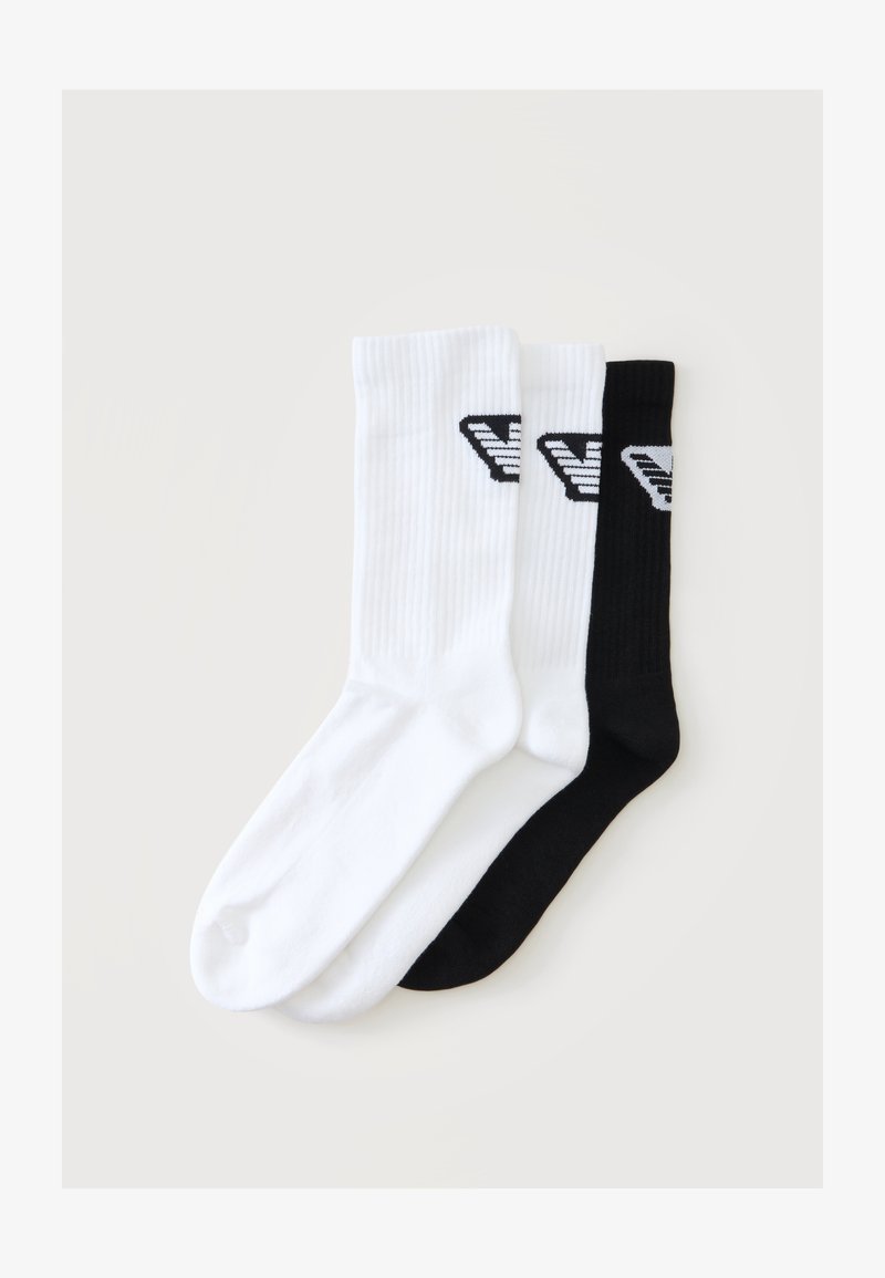 Deux chaussettes blanches et une noire longueur mollet avec une texture côtelée et un logo noir près du haut, disposées côte à côte sur un fond clair.