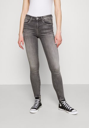 Slim-fit vervaagde grijze jeans gedragen met zwarte hoge sneakers en een wit mouwloos topje, getoond van taille tot voeten.