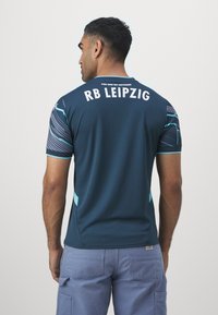 RB Leipzig sötét teal sportmez rövid ujjú, világoskék kiegészítőkkel, oldalsó hálós panelek, és fehér szöveggel a háton.