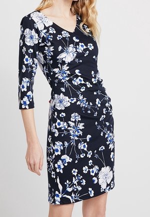 Kukkakuvioinen mekko, jossa on kolmevartiset hihat, V-pääntie ja rypytysdetaili. Tummansininen kangas, jossa valkoisia ja sinisiä kukkakuvioita.