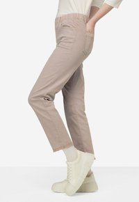 Lichtbeige, elastische broek met zijzakken, rechte pijpen en ruwe zoomafwerking. Gepaard met dikke witte sneakers en witte sokken.