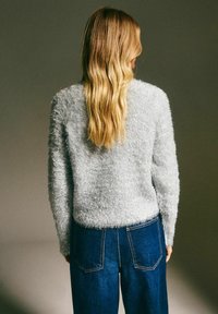 Szary, puszysty sweter z okrągłym dekoltem, długimi rękawami i teksturowanym wykończeniem, w zestawieniu z ciemnoniebieskimi dżinsami z wysokim stanem.