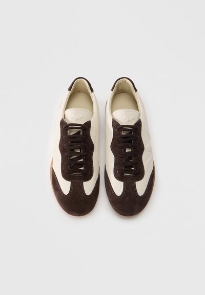 Αθλητικά παπούτσια με επάνω μέρος από εκρού δέρμα και σκούρες καφέ σουέτ λεπτομέρειες. Στρογγυλή μύτη, καφέ κορδόνια και υλικά με υφή. Σχεδίαση χαμηλού ύψους.