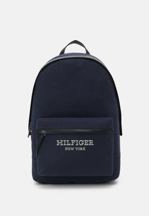 Zaino in tessuto navy con forma curva, tasca frontale con zip, dettagli neri e logo bianco "HILFIGER NEW YORK". Texture liscia, design minimal.