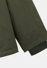 Manche de veste vert olive au toucher lisse, avec un poignet en maille noir contrastant et des coutures soignées le long du bord.