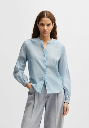 Lichtblauwe blouse met lange mouwen, knoopsluiting, ronde kraag en geplooide manchetten. Zachte stof met een gladde textuur en een relaxte pasvorm.
