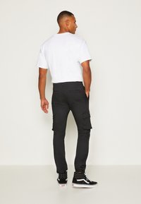 Zwarte cargo broek met klepzakken en een slim fit, gecombineerd met een eenvoudig wit T-shirt. Zwarte high-top sneakers maken de outfit compleet.