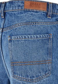 Blå jeans av denim med en läderlapp märkt "URBAN CLASSICS," med orange sömmar och en design på bakfickan.
