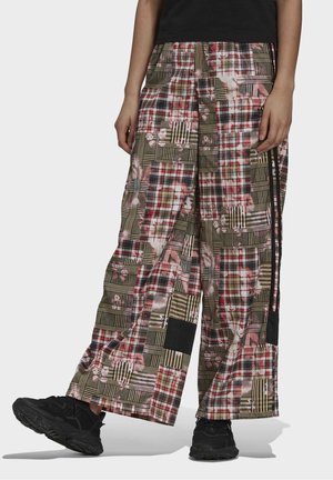 Spodnie typu szerokie nogawki w stylu patchwork w kratę w odcieniach czerwieni, czerni, beżu i oliwki, noszone z czarnymi trampkami i czarnym topem, pokazane od talii do stóp.