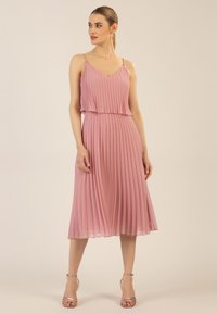 Vaaleanpunainen pleated-mekko, jossa on ohuet hihnat ja V-pääntie. Mekossa on virtaava muotoilu ja kerroksellinen rintaosa. Pehmeä ja kevyt kangas.