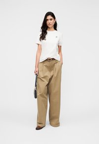 T-shirt blanc à manches courtes avec un petit motif bleu, associé à un pantalon beige ample taille haute, ceinture marron et chaussures marron.