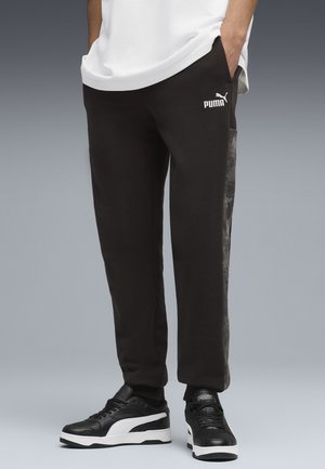 Zwarte joggingbroek met een aansluitend ontwerp, voorzien van een getextureerd zijpaneel en een wit Puma-logo. Gepaard met zwart en witte sneakers.