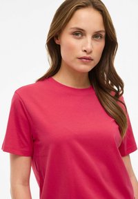 Różowa, krótka koszulka z bawełny o intensywnym kolorze, z okrągłym dekoltem. Gładka faktura, bez widocznych wzorów i zdobień.