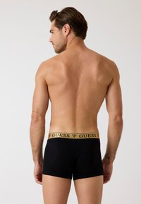 Czarne bokserki z elastycznym, złotym pasem w talii z logo "GUESS", gładkim materiałem i dopasowanym krojem.