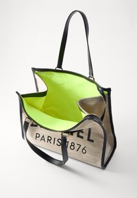 Taška přes rameno s juty vnější vrstvou a černými koženými akcenty. Jasně zelený interiér se zipovým uzávěrem a dvěma pevnými rukojeťmi. Viditelný text "PARIS 1876".