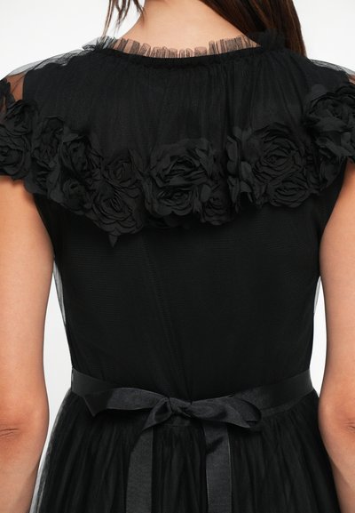 Rochie neagră cu un decolteu din tulle transparent, decorat cu aplicații florale și o curea din satin. Fusta are o textură stratificată cu un design fluid.