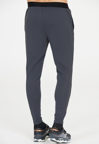 Dunkelgraue Sporthosen mit einer strukturierten Oberfläche, schmaler Passform, elastischem Bund und seitlichen Taschen. Kombiniert mit schwarz-grauen Laufschuhen.