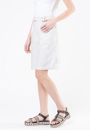 Pantaloni corti in lino color beige chiaro con frontale piatto, tasche laterali e passanti per cintura, abbinati a sandali neri con cinturini e suole intrecciate.