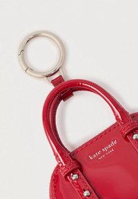 Czerwona mini torebka z lakierowanej skóry jako brelok do kluczy z metalowym srebrnym pierścieniem i logo "kate spade NEW YORK" na przedniej stronie.