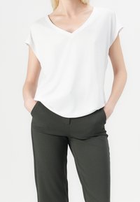 Bílý tričko s výstřihem do V a krátkými rukávy, hladká textura, v kombinaci s tmavě zelenými elegantními kalhotami. Úzký střih s bočními kapsami.