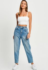 Top corto blanco con diseño texturizado, combinado con jeans de fason alto de mezclilla azul claro. El modelo lleva zapatillas blancas.