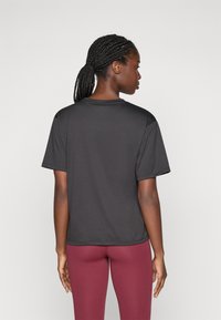 T-shirt noir à manches courtes avec un col rond. Texture lisse, coupe standard. Porté avec des leggings bordeaux, sur un fond neutre.