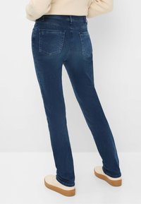 Jeans in denim blu scuro con una vestibilità dritta, caratterizzati da due tasche posteriori e dettagli di cucitura sottili, abbinati a sneaker piatta di colore chiaro.
