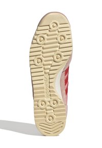 Sola della scarpa sportiva caratterizzata da una gomma cremoso testurizzata con elementi di trazione circolari; materiale scamosciato rosa con strisce rosse sui lati.