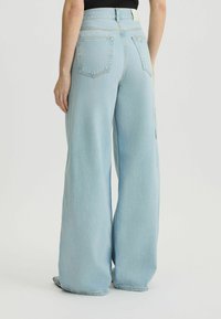 Jeans de pernera ancha de color azul claro con una cintura alta, cinco bolsillos y costuras a contraste. Tejido de denin suave con una textura lisa y un diseño sin adornos.