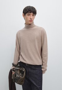 Beige turtleneck sweater made of soft material, paired with dark denim jeans and holding a dark leather bag with metal accents.