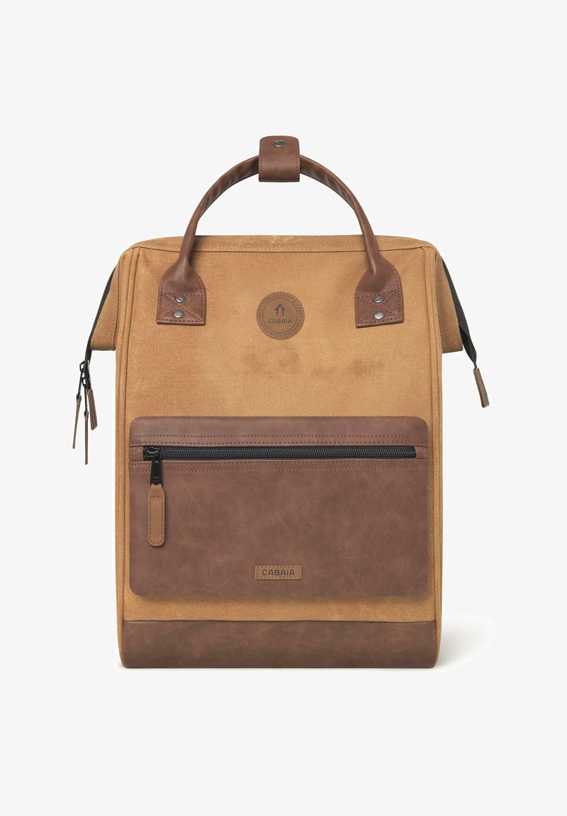 Sac à dos en toile beige avec des accents en cuir marron, doté d'une poignée supérieure, d'une poche zippée à l'avant et d'un patch logo rond. Détails des zips et des coutures.