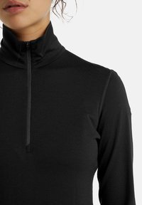 Black long-sleeve shirt with a high collar and quarter zip. Smooth, stretch fabric with minimal seams, close-fitting design.