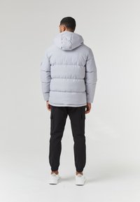 Light gray puffer jacket with a hood, featuring horizontal stitching and a relaxed fit, paired with black cargo pants and white sneakers.