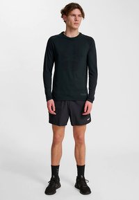 Svart långärmad atletisk topp med rund halsringning, kombinerad med mörka shorts. Tyget verkar slätt och lätt, lämpligt för sport.