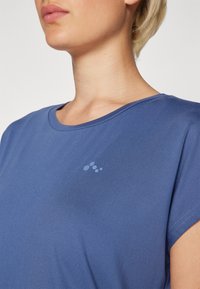 Blue short-sleeve shirt made of smooth fabric, featuring a rounded neckline, and a subtle logo on the left chest area.
