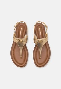 Ζευγάρι καφέ και χρυσών σανδαλιών Michael Kors με λουριά στον αστράγαλο και λεπτομέρεια λογότυπου, σε λευκό φόντο, φωτογραφημένο από πάνω.