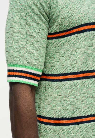 Zelený pletený sveter s krátkym rukávom a textúrovaným štvorcovým vzorom, s oranžovo-modro-bielo-zelenými pruhmi na rukávoch a tele.