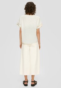 Hellbeige Oversized-Top mit kurzen Ärmeln, kombiniert mit weit geschnittenen, hellbeigen Hosen. Schwarze Plateausandalen vervollständigen den Look.
