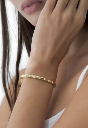 Bracciale in oro con bangles caratterizzato da pietre chiare di forma rettangolare e rotonda, superficie liscia e finitura lucida, indossato su un polso.