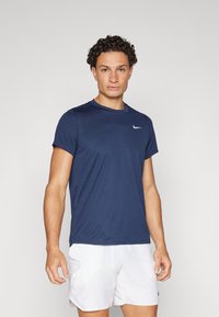 Camisola atlética de manga curta azul-marinho com decote redondo e logótipo da Nike em branco. Têxtil suave, tecido leve, combinado com calções brancos.