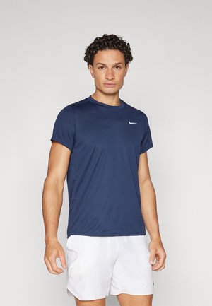 Maglietta atletica a maniche corte di colore blu navy con colletto rotondo e logo Nike bianco. Tessuto liscio, leggero, abbinata a pantaloni shorts bianchi.