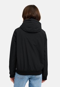 Črna kapuca z ohlapnim krojem, elastičnim pasom in manšetami, izdelana iz gladkega materiala, s preprostim, minimalističnim dizajnom.