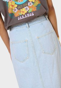 Falda de mezclilla azul claro con cintura alta, costura trasera y dos bolsillos de parche con costuras amarillas en contraste. Textura suave.