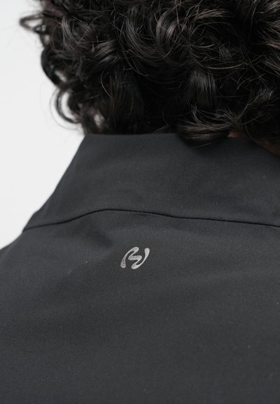 Fekete dzseki gallér nézete, sima szövet textúrával és egy kis ezüst logóval a hátoldalon. Tiszta vonalak és minimalista dizájn.