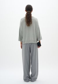 Light gray oversized sweater with a round neckline and wide sleeves, paired with loose-fitting gray trousers, held with a black wallet.